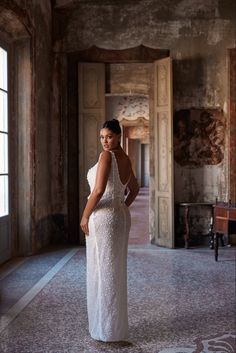 a woman is standing in an old building wearing a white dress and posing for the camera