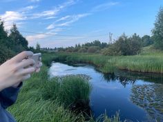 a person holding a cell phone in their hand next to a body of water and grass