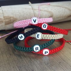 three crocheted bracelets with letters on them sitting on a table next to a piece of fabric