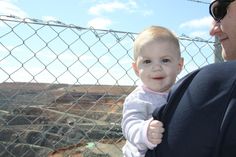 a man holding a baby in front of a chain link fence at the edge of a canyon