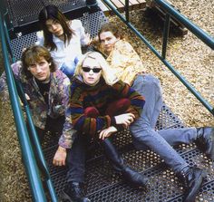 four people sitting on the ground in front of a metal structure with stairs leading up to them