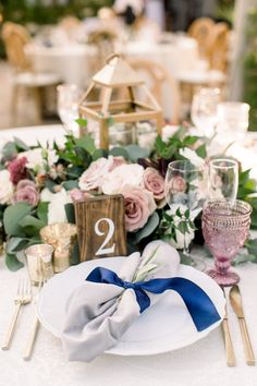 the table is set with white plates and blue napkins, gold place settings, silverware, and pink flowers