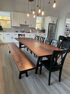 a dining room table and bench in a kitchen with white cabinets, wood floors and light bulbs hanging from the ceiling