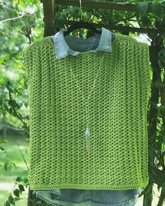 a green crocheted shirt hanging on a clothes line in front of a tree