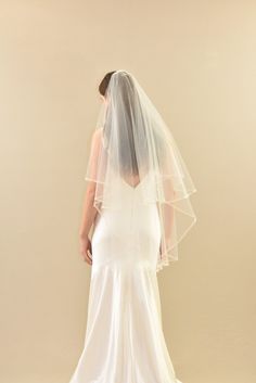 the back of a woman wearing a white wedding dress with a veil on her head