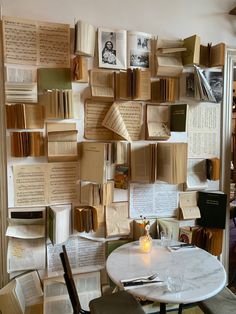 many books are stacked on the wall above a table with a candle and some glasses