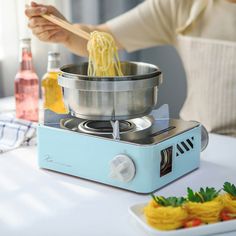 a woman stirring noodles in a pot on top of an electric stove with a wooden spoon