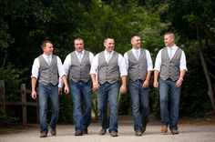 a group of men walking down a road next to each other in jeans and vests