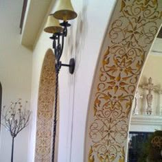 an ornate design is on the wall next to a lamp and mirror in a room