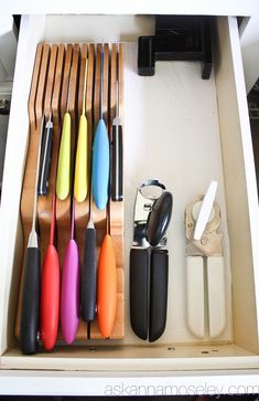 a drawer filled with different colored kitchen utensils and knives on top of each other