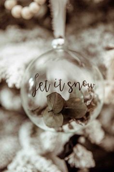 a glass ornament with the word let it snow written on it and leaves inside