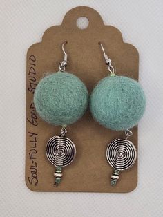 the earrings are made out of yarn and silver metal wire, with green beads on each ear