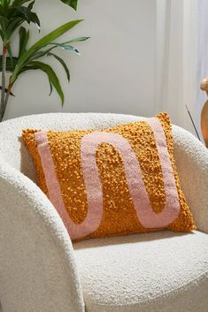 a white chair with a yellow and pink pillow on it next to a potted plant