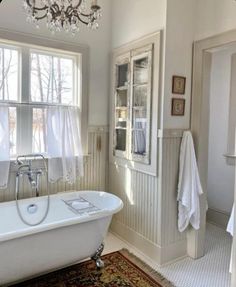 a white bath tub sitting under a window next to a sink in a bathroom with a rug on the floor