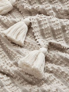 white crocheted blanket with tassels laying on top of eachother