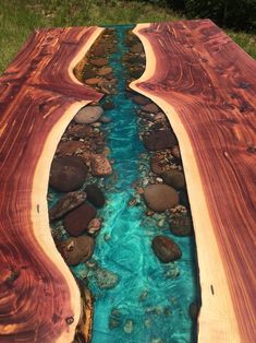 a wooden table with blue water and rocks in the bottom half, on top of green grass