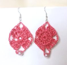 pink crocheted earrings with pearls hanging from them on a white surface, ready to be worn