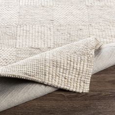 a white rug on top of a wooden floor next to a gray and white blanket