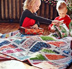 two young children playing with a quilt on the floor in front of a christmas tree