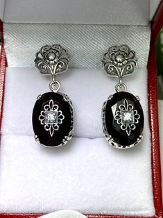 Faux Black Onyx Solid Sterling Silver Earrings Edward Embellished Design#E70e This is a pair of antique-inspired Edwardian style earrings. The flawless oval simulated black onyx gems are surrounded by delicate sterling silver filigree. The lovely full cut oval stones are approximately 14mm x 10mm. In the middle of each earring there lies delicate filigree surrounding a centered inset gem. Please choose white CZ (cubic zirconia), Lab Moissanite, or genuine diamond for the inset gem. The earrings Elegant Black Oval Earrings, Black Oval Earrings For Formal Occasions, Elegant Black Filigree Earrings, Black Oval Pierced Earrings, Black Filigree Earrings, Formal Black Filigree Earrings, Antique Black Drop Earrings, Black Antique Drop Earrings, Black Oval Vintage Earrings