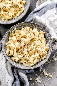 two bowls filled with pasta and parmesan cheese on top of a gray table