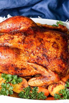 a roasted turkey with carrots and parsley in a white dish on a blue cloth