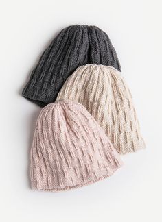 three knit beanies sitting next to each other on a white surface, one black and one pink