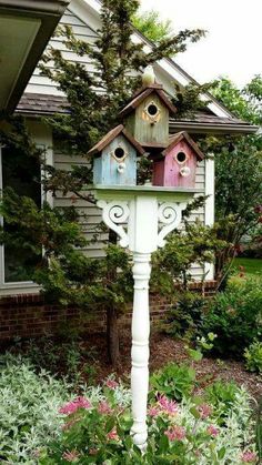 a white bird house sitting on top of a pole in the middle of flowers and trees