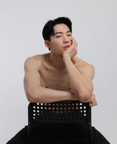 a shirtless man sitting in a chair with his hand on his chin