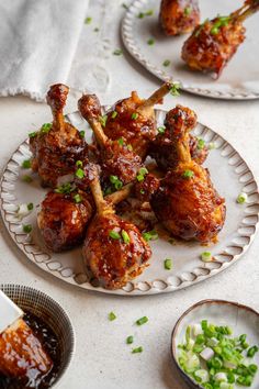 chicken wings with sauce and green onions on a white plate next to small bowls filled with condiments