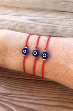 three red string bracelets with evil eye beads on the wrist and an evil eye bead