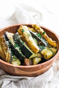 a wooden bowl filled with zucchini on top of a white cloth next to a fork