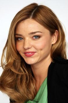 a woman with long, wavy hair and blue eyes smiles at the camera while wearing a green shirt