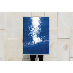 a person holding up a large blue piece of art in front of a white wall