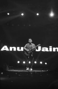 a man standing on top of a stage with an acoustic guitar in front of him