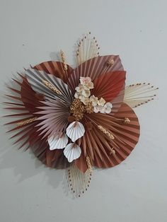 a decorative wall hanging made out of paper flowers and fan shaped leaves on a white wall