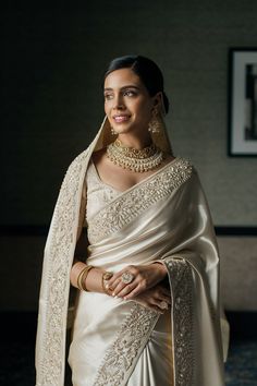 a woman in a white sari and gold jewelry poses for the camera with her hand on her hip