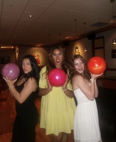 three women in dresses are holding balloons and posing for the camera with their mouths open