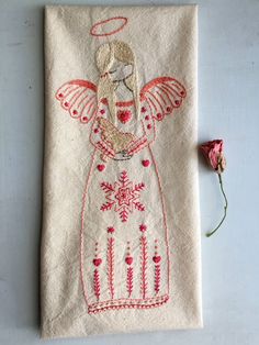 an embroidered angel on a white cloth with pink flowers