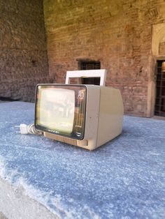 an old tv sitting on top of a stone table next to a brick wall and doorway