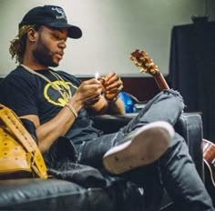 a man sitting on top of a couch holding a guitar and looking at his cell phone