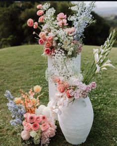 two white vases with flowers are on the grass