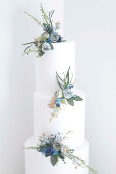 three tiered white wedding cake with blue flowers and greenery