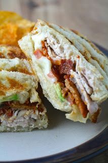 a sandwich cut in half sitting on top of a white plate next to potato chips