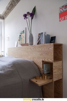 a bed with a wooden headboard and shelves on the wall next to it that have flowers in vases