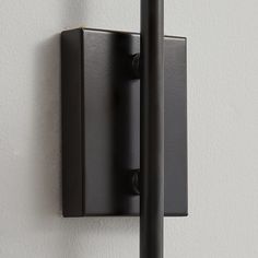 a black wall light mounted on the side of a white wall next to a pole