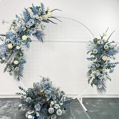 an arrangement of blue and white flowers arranged in a circle on a metal stand against a wall