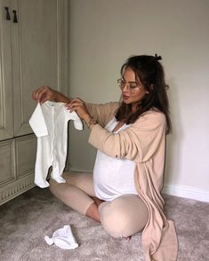 a pregnant woman is sitting on the floor and holding a baby's clothes in her hands