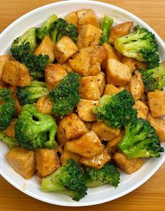 a white bowl filled with broccoli and chicken on top of a wooden table