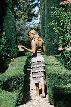 a woman standing in the middle of a garden looking at her cell phone while wearing a dress